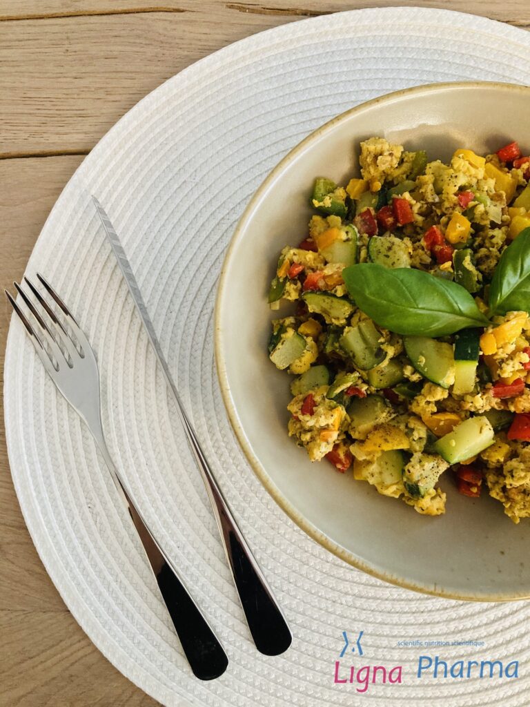 Een kleurrijke omelet met champignons, courgette, rode en gele paprika, afgewerkt met verse basilicumblaadjes. Het gerecht is geserveerd op een beige bord met lichte placemat – een gezonde, eiwitrijke maaltijd die perfect past binnen het Infraligne en Ligna Pharma dieet.