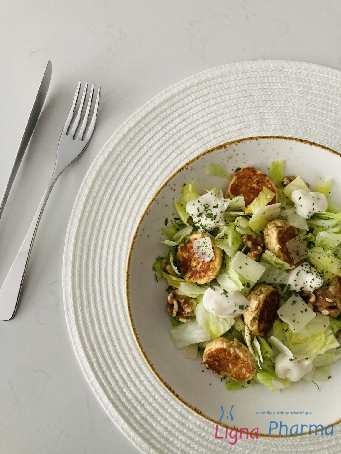 Een frisse salade met vegetarische kipnuggets, ijsbergsla, komkommer, parmezaanschilfers, walnoten en een toefje dieetmayonaise, gepresenteerd op een wit bord met stijlvolle opmaak. Een lichte, eiwitrijke maaltijd die past binnen het Infraligne en Ligna Pharma dieet.