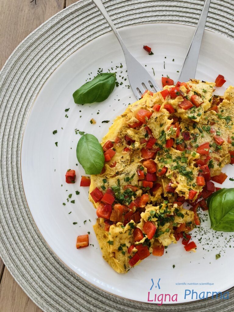 Een kleurrijke Mediterraanse omelet met rode paprika, bieslook en verse basilicum op een wit bord. Het gerecht straalt gezondheid en balans uit – een lichte, eiwitrijke maaltijd die perfect past binnen het Infraligne en Ligna Pharma voedingsplan.